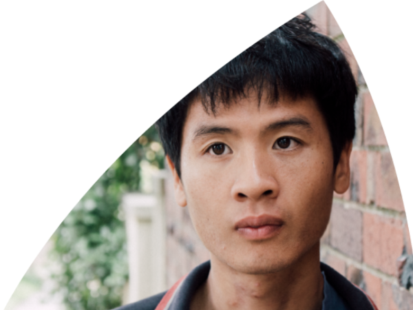 A young man leaning against a brick wall looks off camera