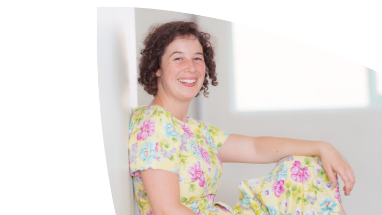 A young woman in a floral dress smiles at the camera