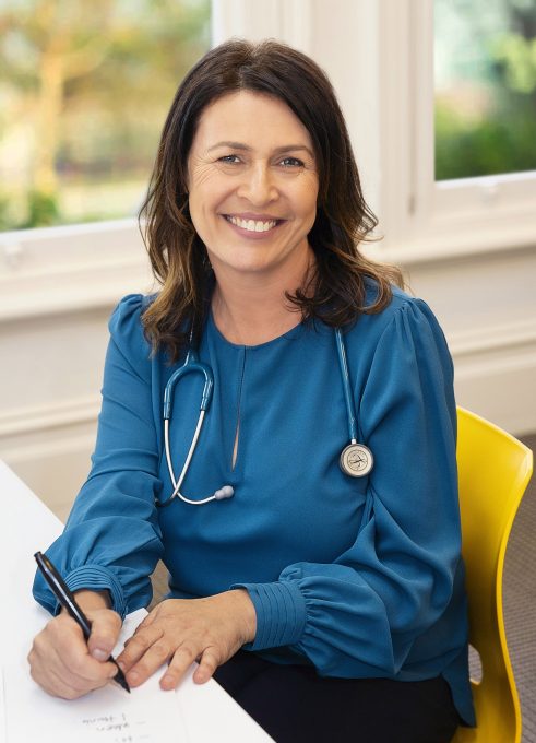 A woman smiling in a blue shirt with a stethoscope around her neck